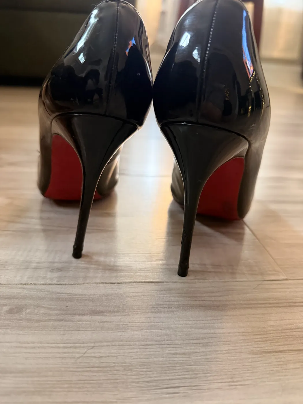 A pair of black patent stiletto heels with red soles, after repair